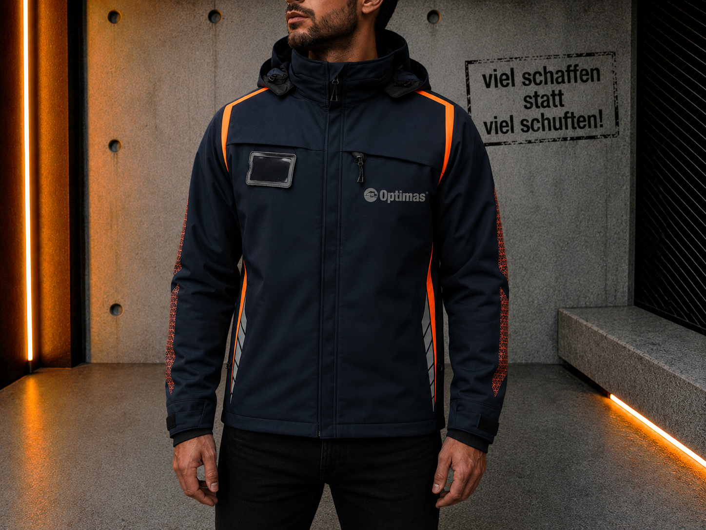 Ein Mann in einer dunkelblauen Jacke mit orangefarbenen Akzenten steht vor einer strukturierten Wand und präsentiert moderne Arbeitskleidung – Optimas.