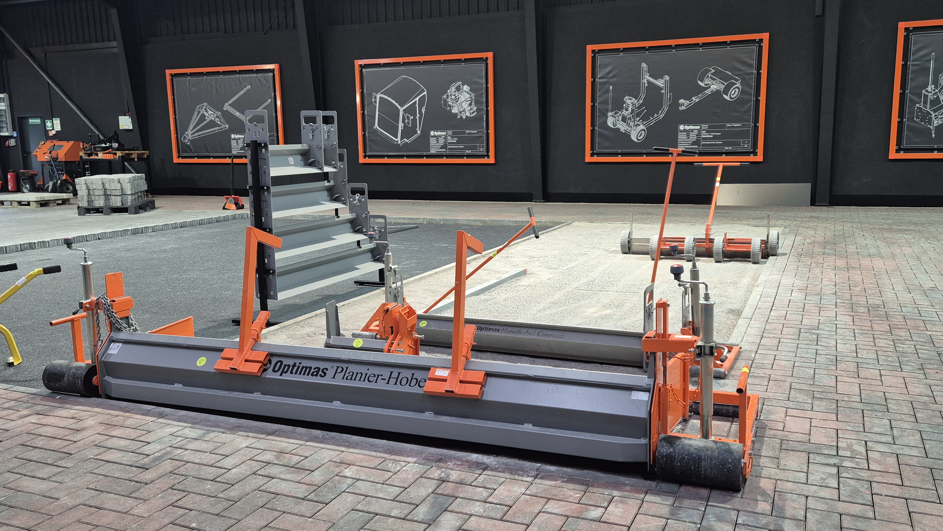 Eine Lagerhalle mit einer Maschine zum Pflastern mit orangefarbenen Akzenten, umgeben von technischen Zeichnungen – Optimas.