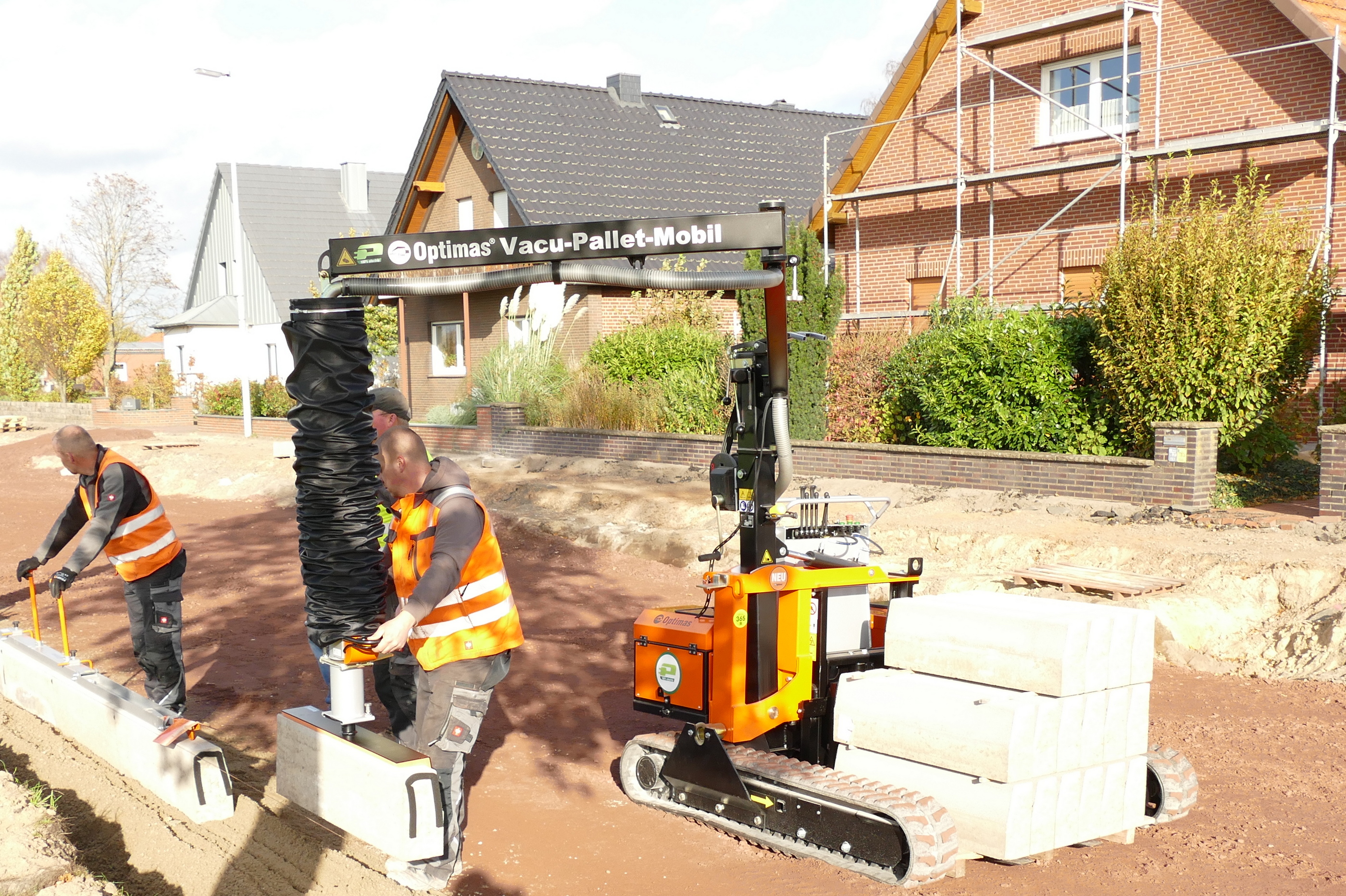Arbeiter nutzen ein Optimas Vacu-Pallet-Mobil, um Betonblöcke für ein Pflasterprojekt in einem Wohngebiet zu heben und zu platzieren, und präsentieren dabei Pflastergeräte – Optimas.
