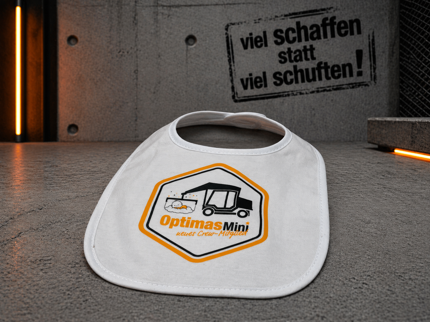 Ein weißes Lätzchen mit dem Optimas Mini-Logo auf einer strukturierten Oberfläche mit motivierendem Hintergrund – Optimas.