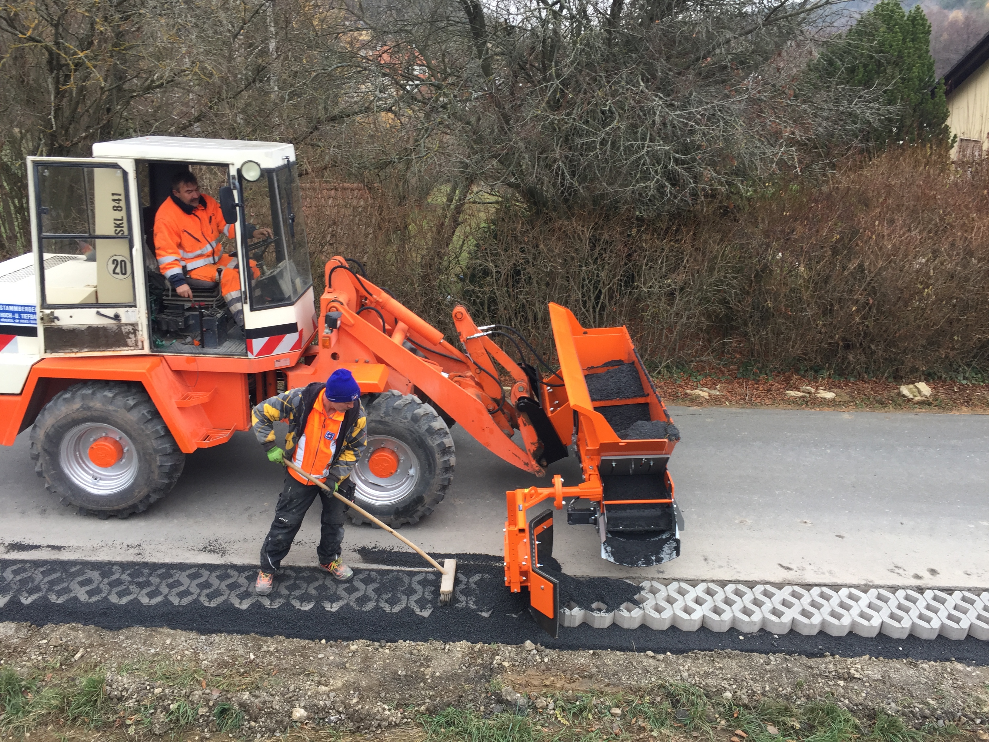 Bauarbeiter füllen mit einer orangefarbenen Maschine Lücken zwischen Pflastersteinen mit Asphalt und sorgen so für glatte Oberflächen und verbesserte Stabilität – Optimas.