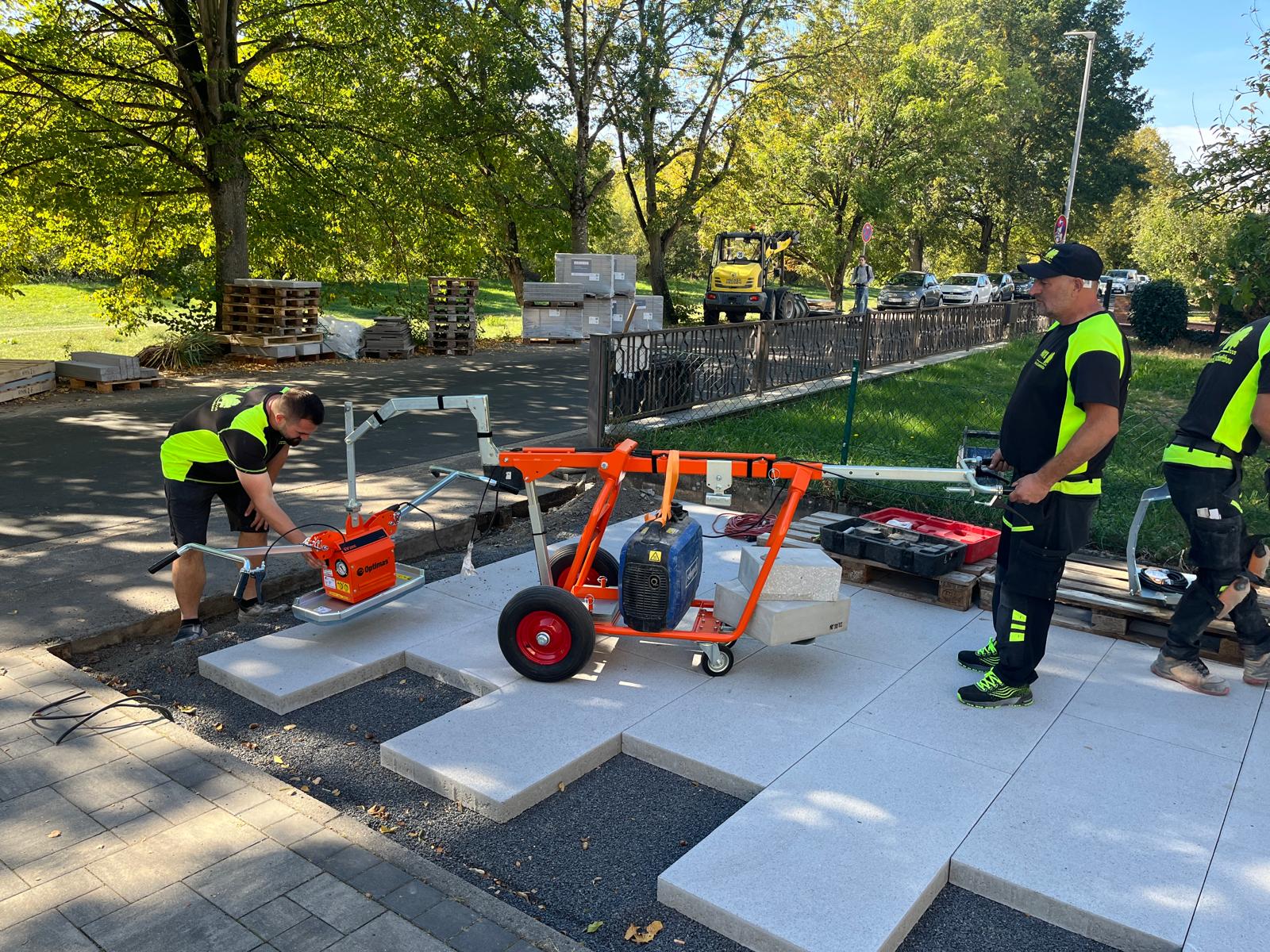 Arbeiter verlegen mit einem Optimas SV-Verlegewagen mit Vakuumgerät große Betonpflastersteine ​​im Außenbereich – Optimas