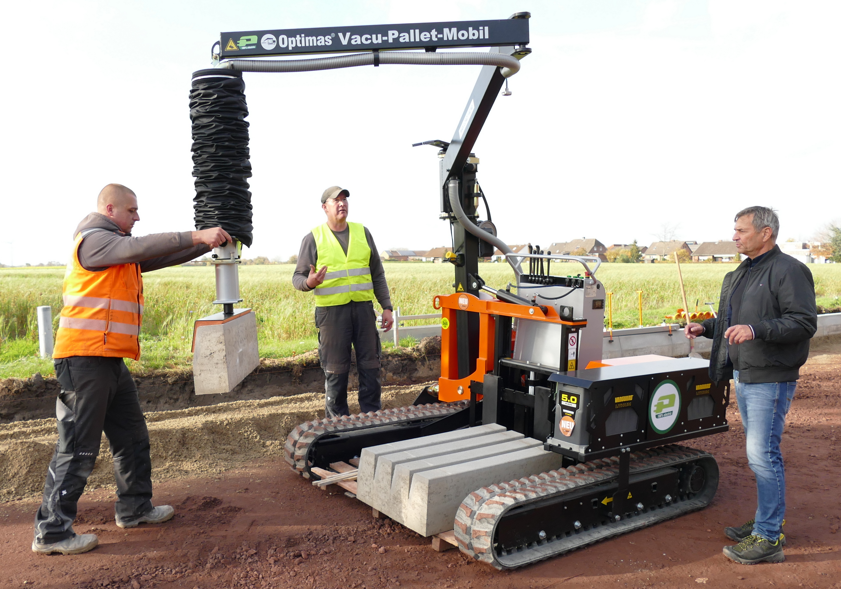 Die von drei Bauarbeitern bediente Optimas Vacu-Pallet-Mobil-Maschine verfügt über Raupenräder und einen Vakuum-Hebearm zum Bewegen von Betonblöcken – Optimas.