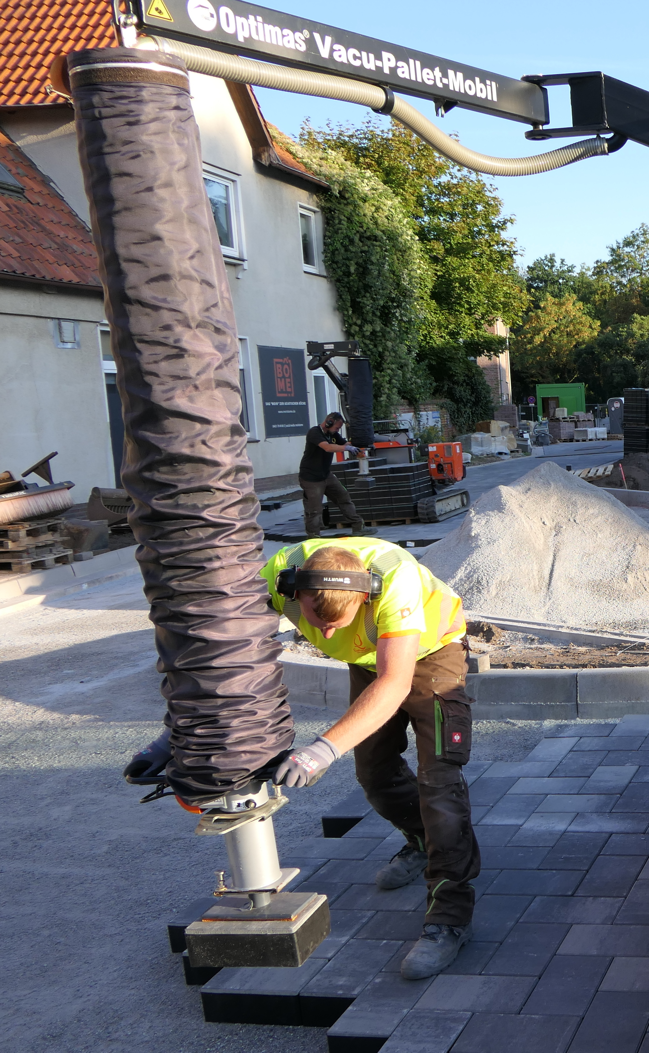 Ein Arbeiter nutzt das Optimas Vacu-Palettenmobil zum Positionieren von Pflastersteinen auf einer Baustelle – Optimas.