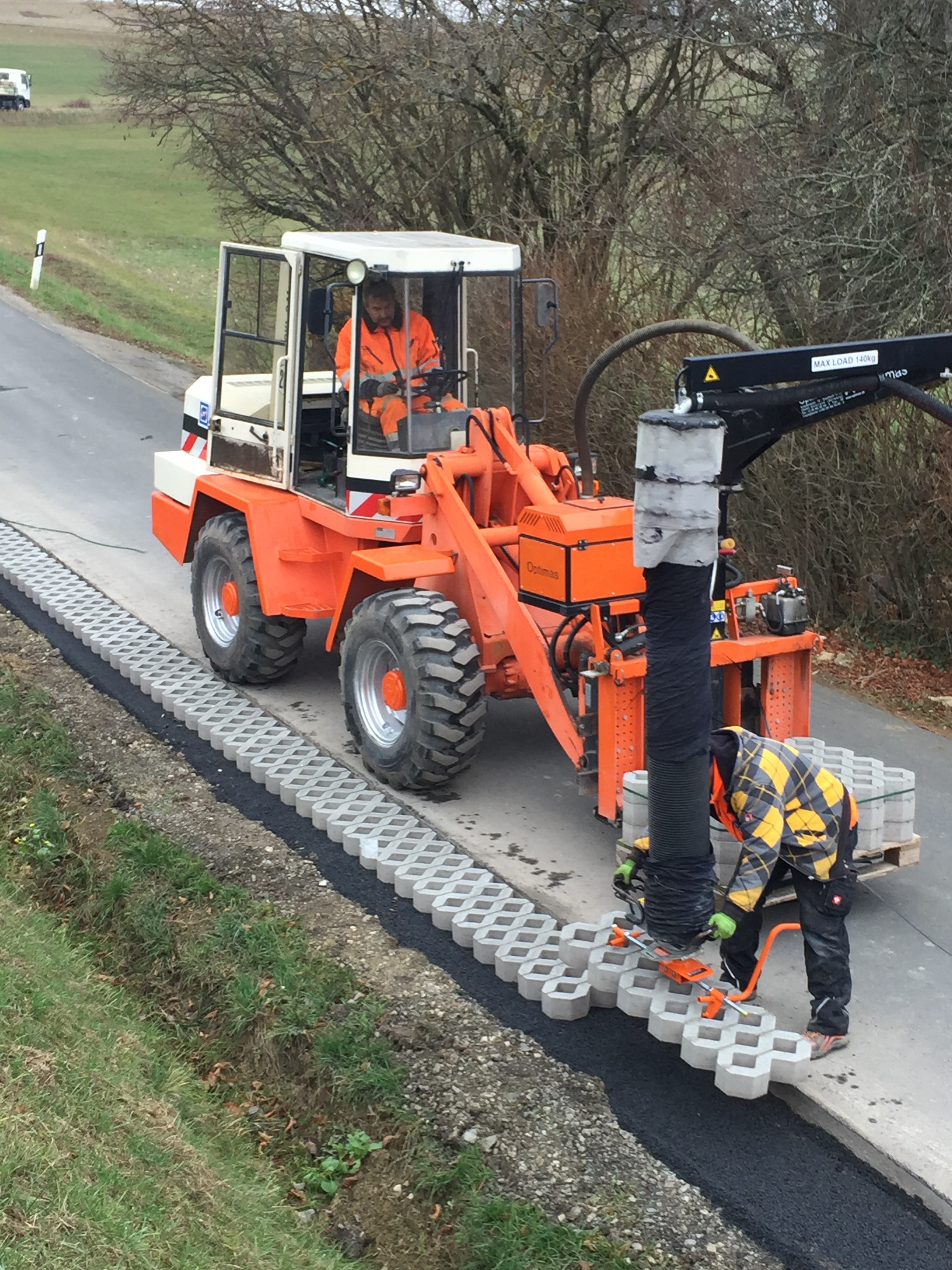Arbeiter installiert Betonblöcke mit einer Optimas-Maschine auf einer Straße und präsentiert Baumaschinen und laufende Straßenarbeiten für den Landschaftsbau – Optimas.