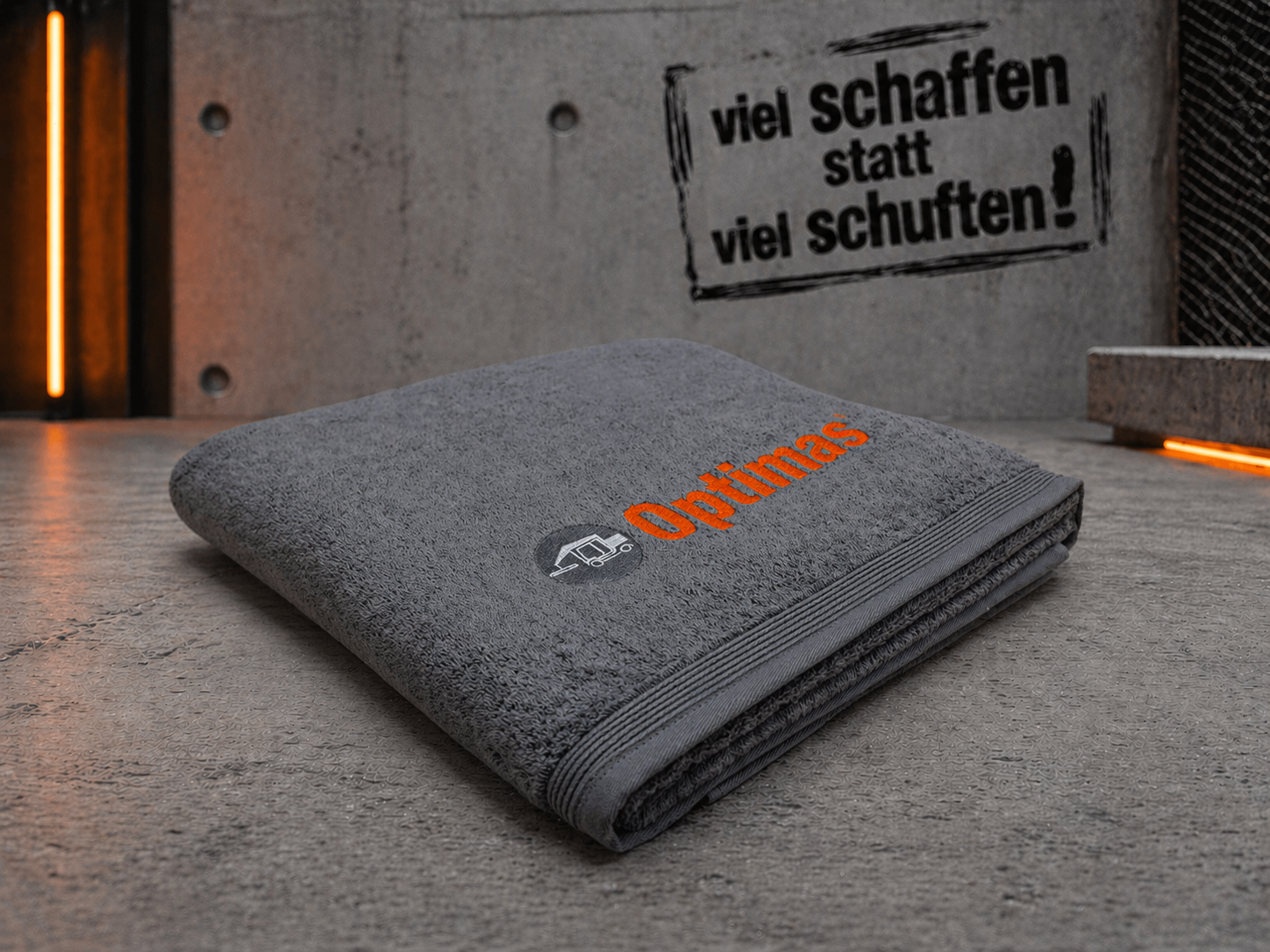 Une serviette grise pliée avec le mot « Optimas » brodé en orange sur une surface texturée – Optimas.