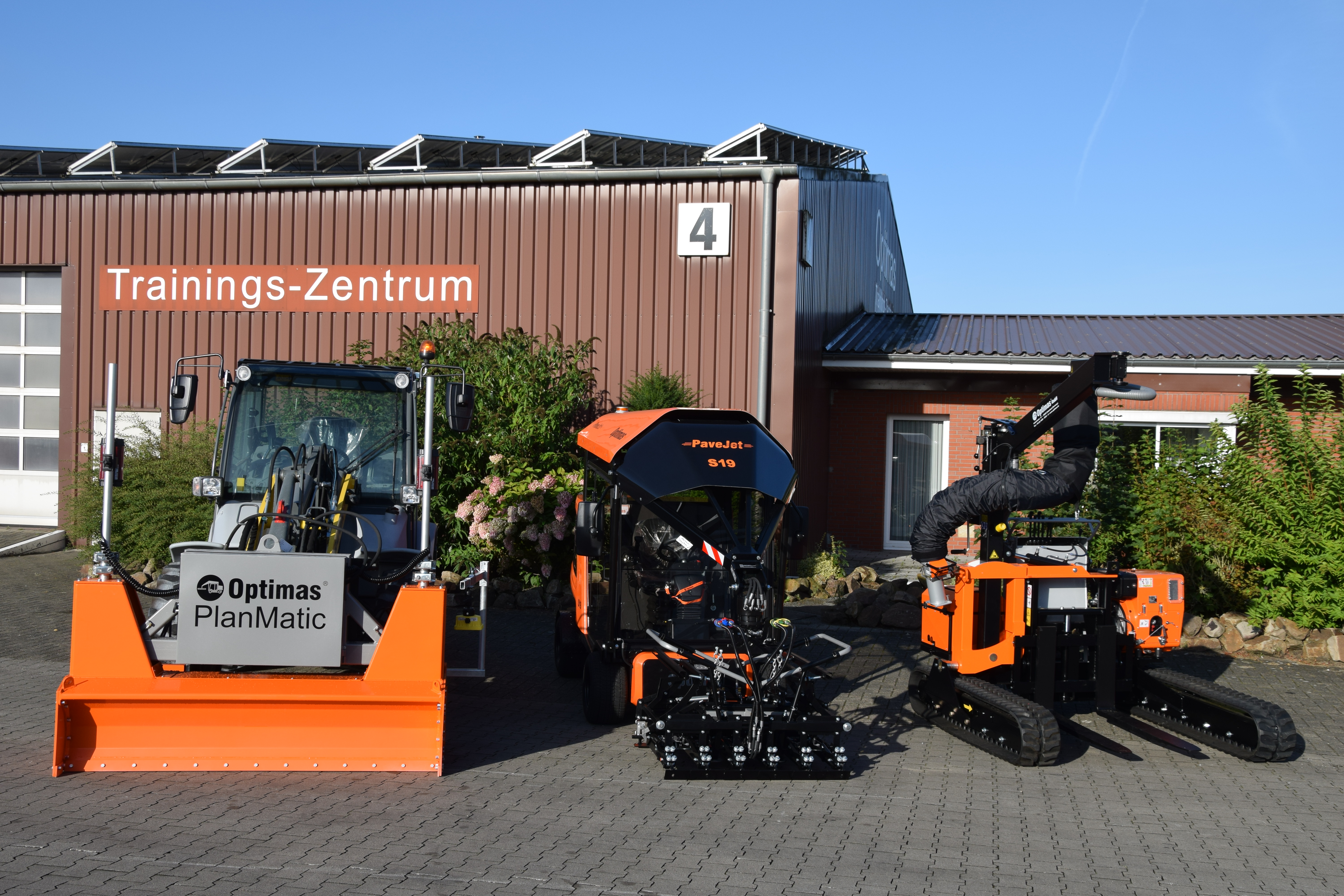 Die Pflastermaschinen Optimas PlanMatic und PaveJet S19 parken vor dem Schulungszentrum und präsentieren fortschrittliche Baumaschinen – Optimas.