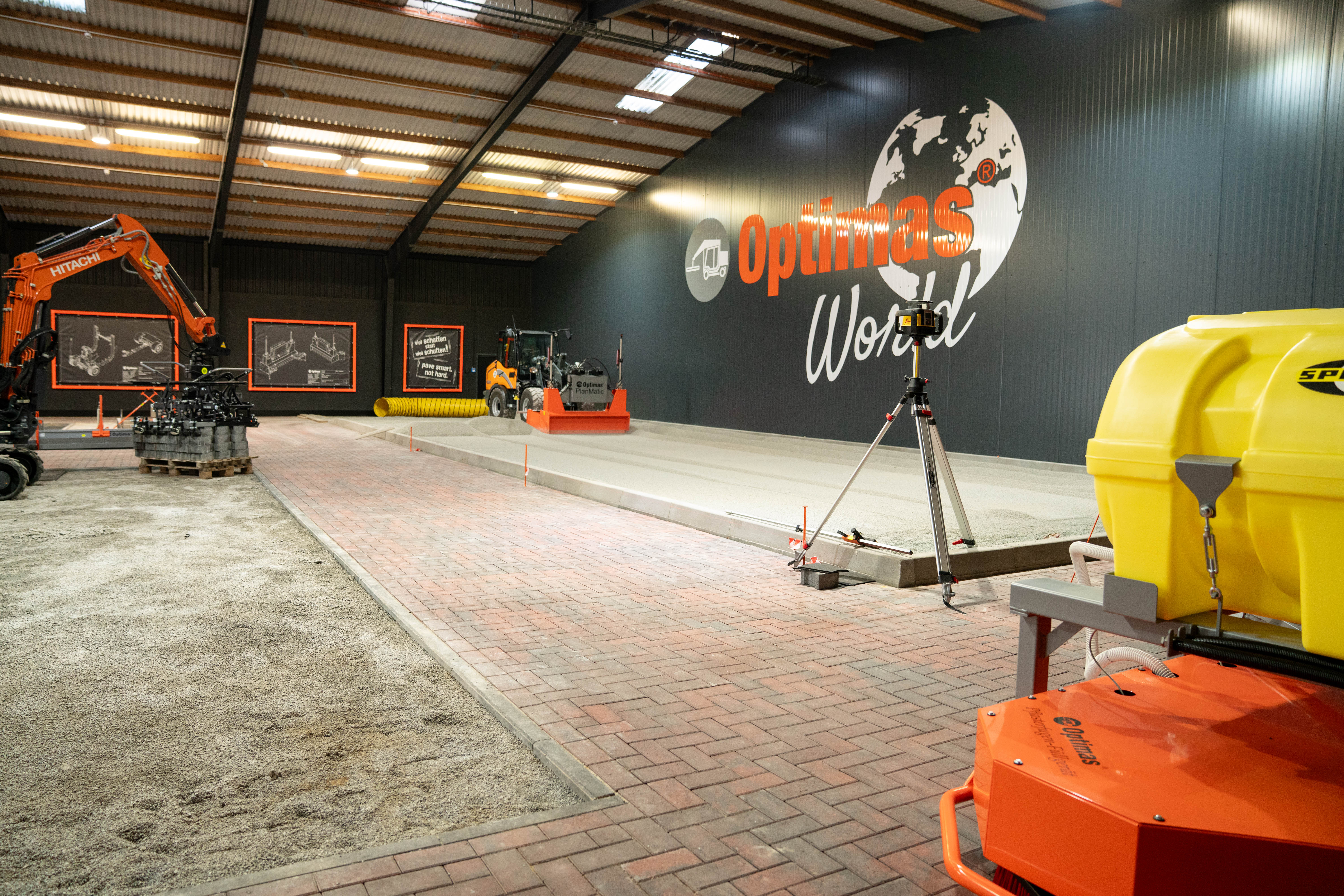 Ein Indoor-Baubereich mit Maschinen, Werkzeugen und einer Wand mit dem Optimas-Logo – Optimas.