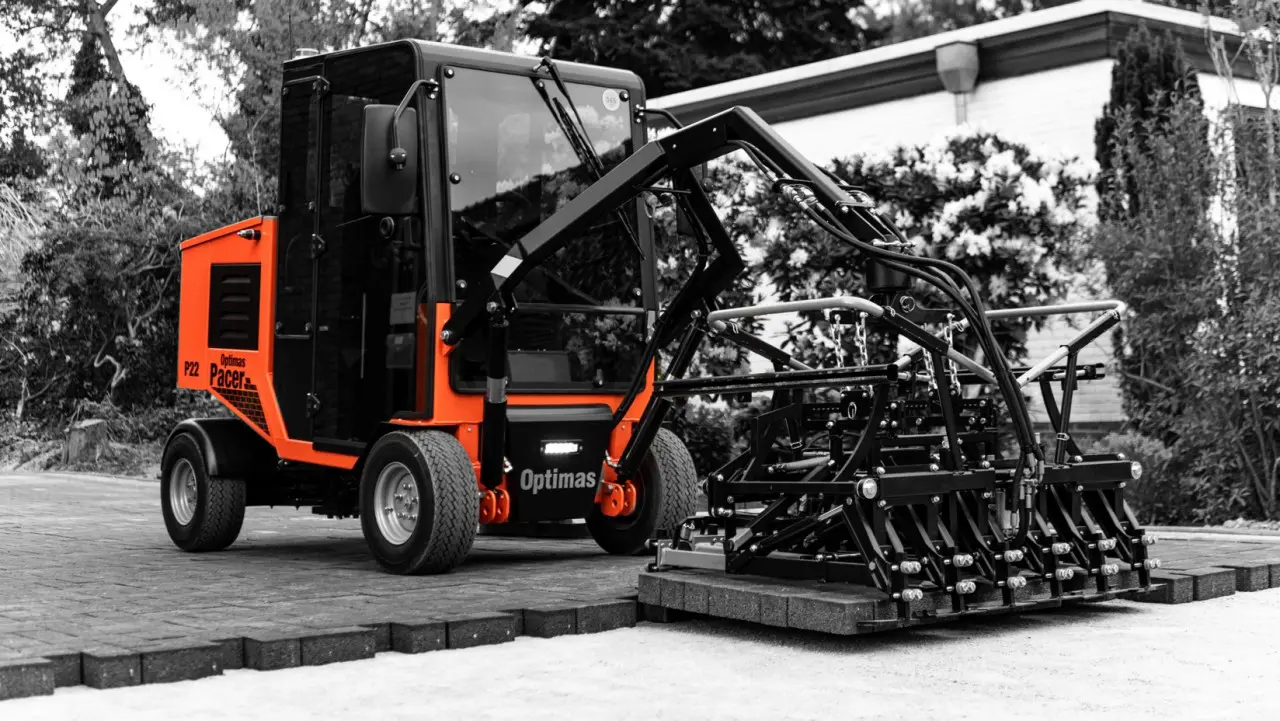 Ein kompaktes Baufahrzeug im orange-schwarzen Design, ausgestattet mit einem Pflasteraufsatz – Optimas.