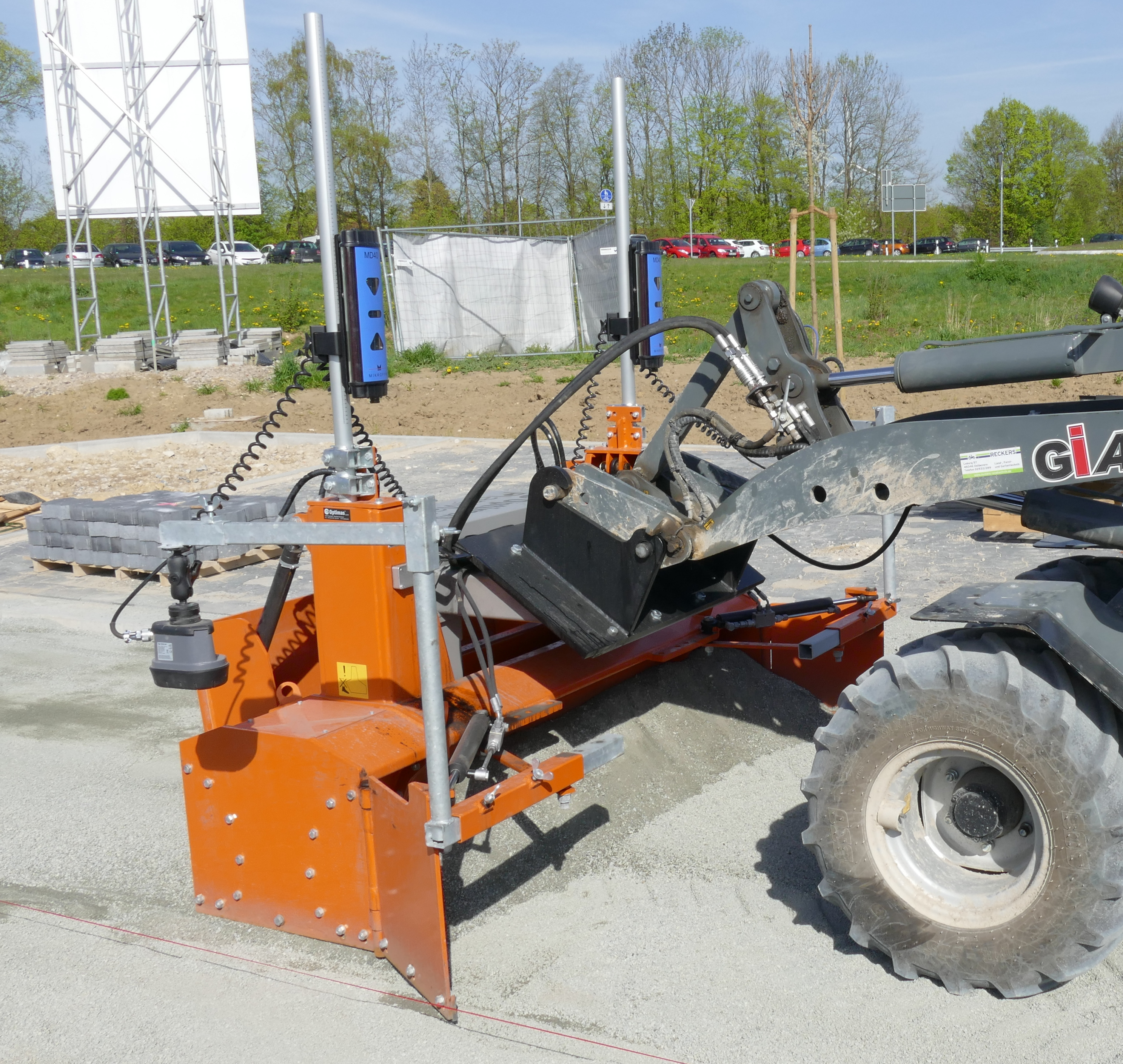 RIESIGE Nivelliermaschine für den Einsatz auf einer Kiesoberfläche, ausgestattet mit Lasersteuerung für präzises Planieren und Nivellieren im Freien während des Baus – Optimas.