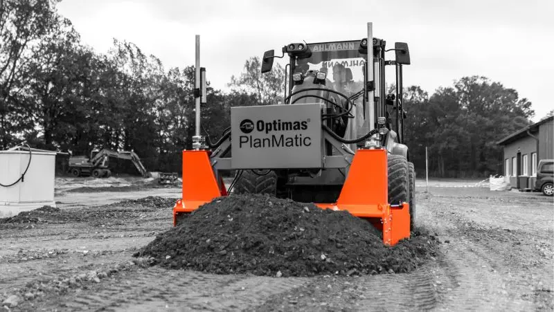 Ein Baufahrzeug mit orangefarbenem Anbaugerät, das Erde auf einer Baustelle bewegt – Optimas.