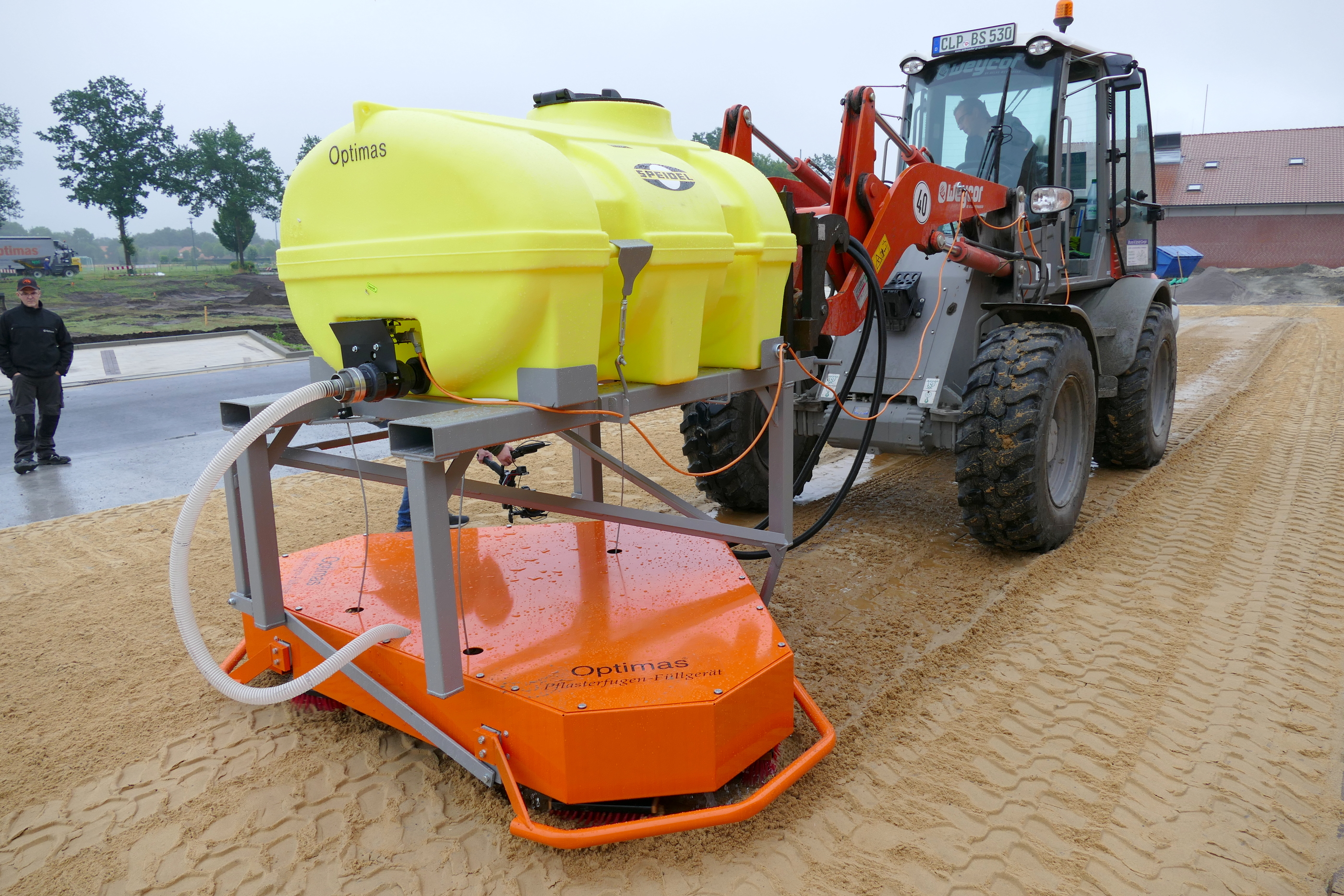Optimas Pflasterfugen-Füllgerät im Einsatz, mit leuchtend gelbem Tank und orangefarbenem Verteiler für eine glatte Oberfläche – Optimas.
