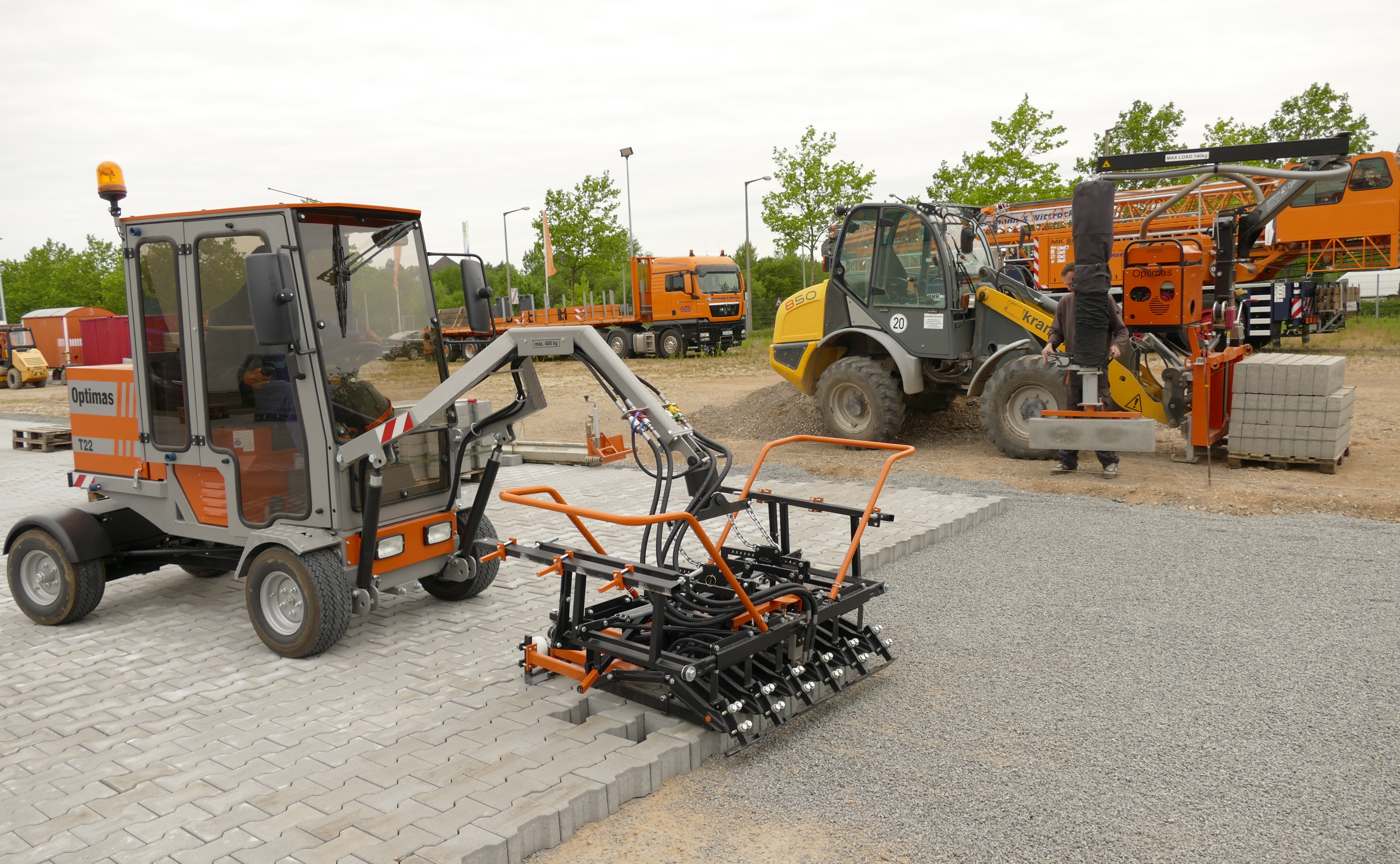 Das Bild zeigt Straßenbaumaschinen, darunter Optimas T22 und 850, auf einer Baustelle, mit sichtbaren LKWs und anderen Geräten, Optimas – Optimas.